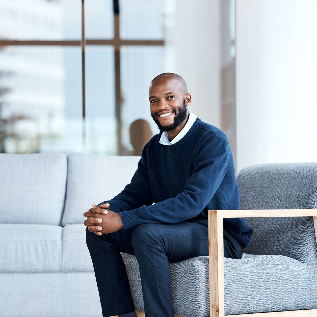 Businessman, happy and smiling at work, job or modern workplace sitting in waiting room for interview at office building. Portrait, employee and African American worker with positive mindset