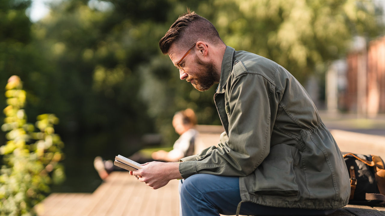 Man reading a paperback book in a public park