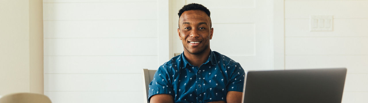 A 30 year old man works on his finances at his kitchen table. He is working on his bank account numbers and preparing to pay his taxes. He is happy, positive and looking forward to better financial times