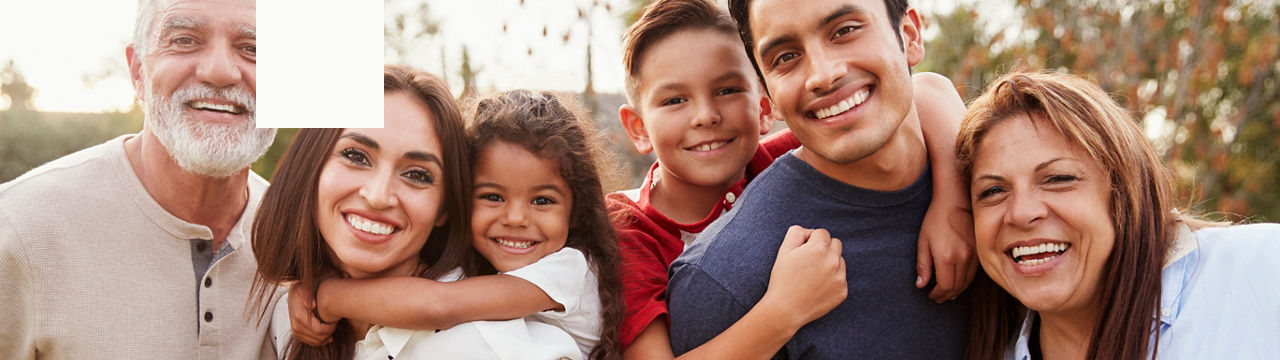 Three generation Hispanic family standing in the park, smiling to camera, selective focus